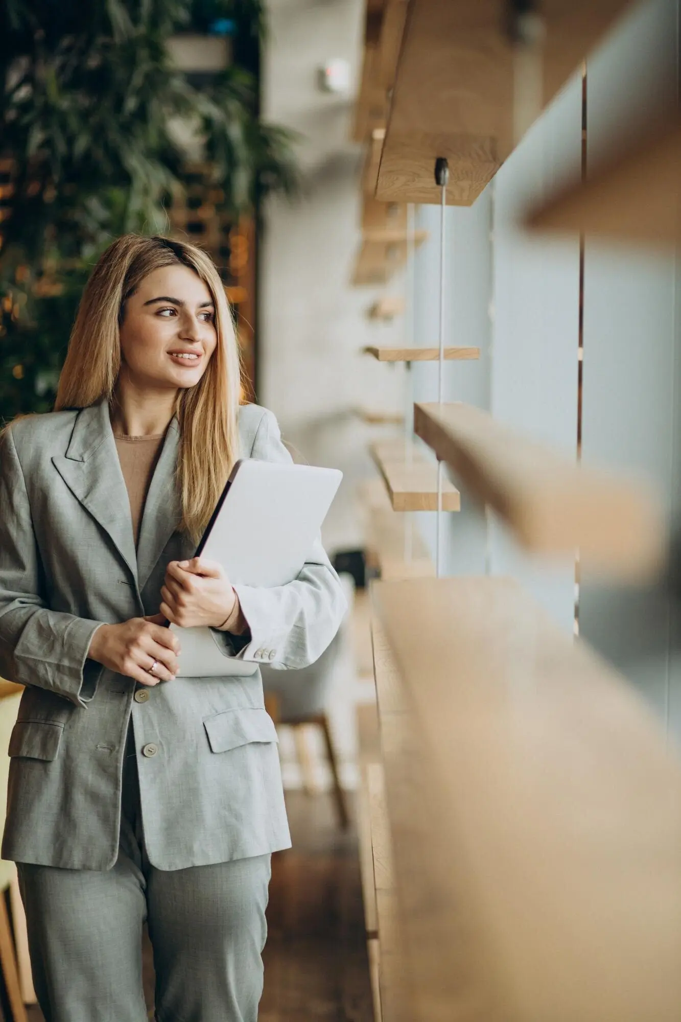 A businesswoman stands by the window, holding a computer.