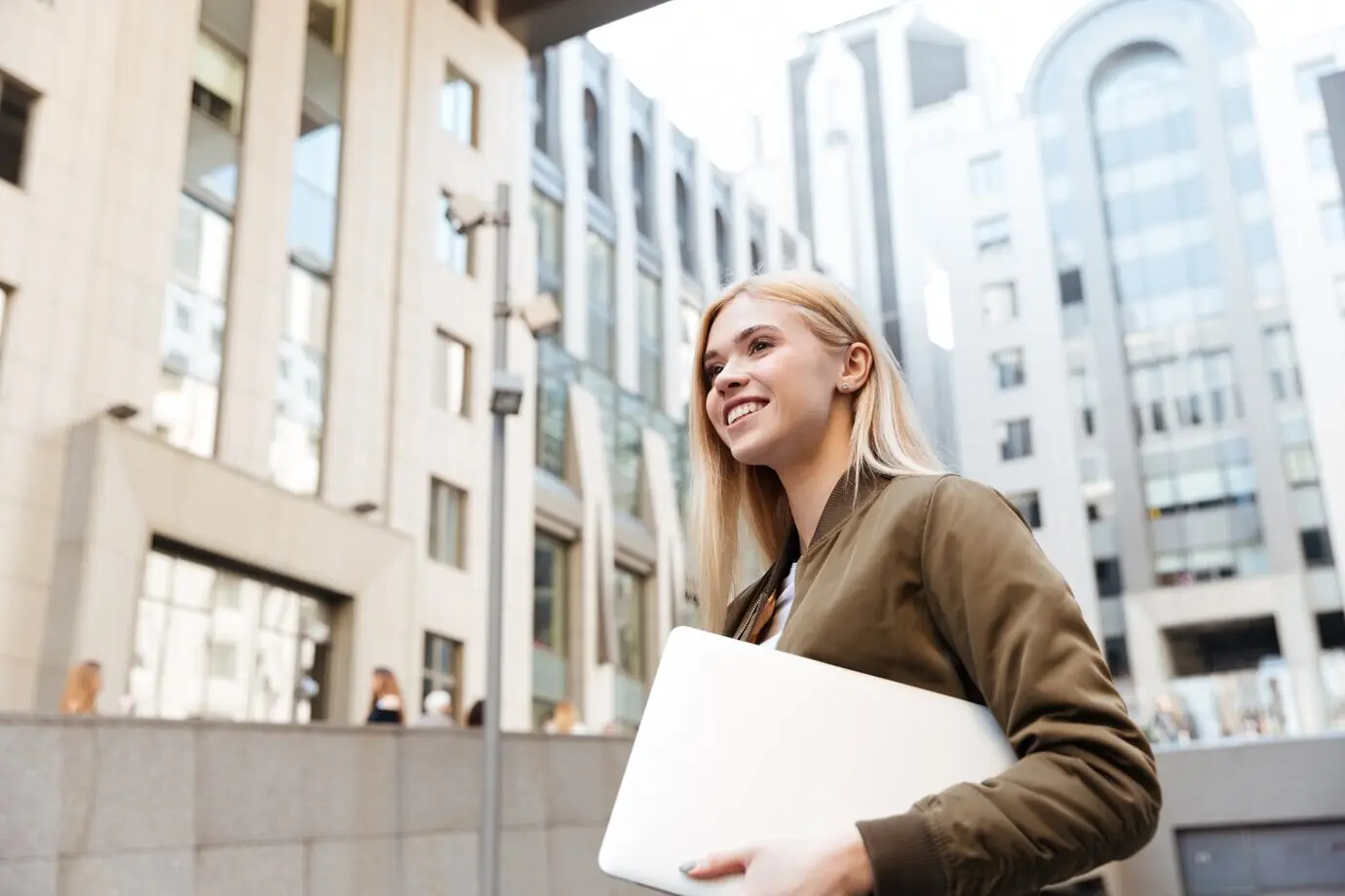 A young woman with a laptop computer walks in the street.